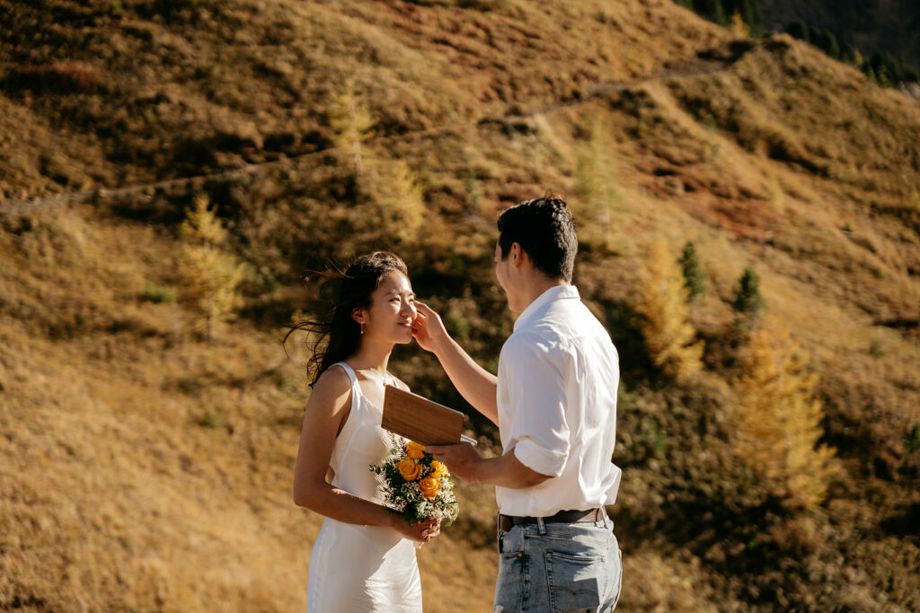 Couple exchanging vows outdoors by autumn hillside.