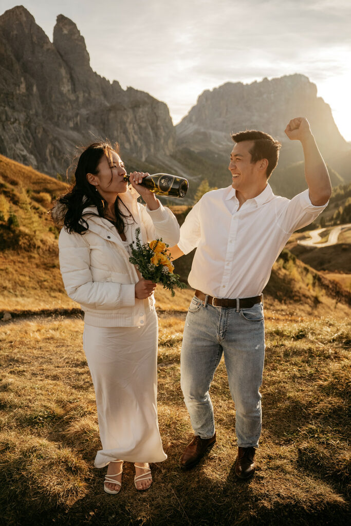 Couple celebrating with champagne in scenic mountain landscape.