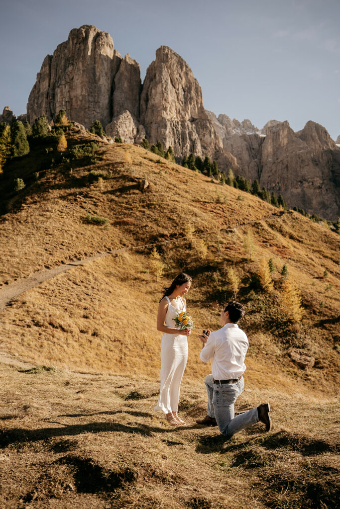 Mountain proposal, man kneeling, woman holding flowers.