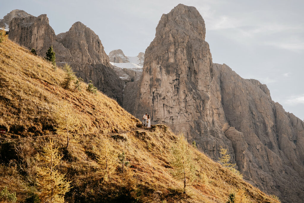 Couple standing on mountain path with cliffs behind.