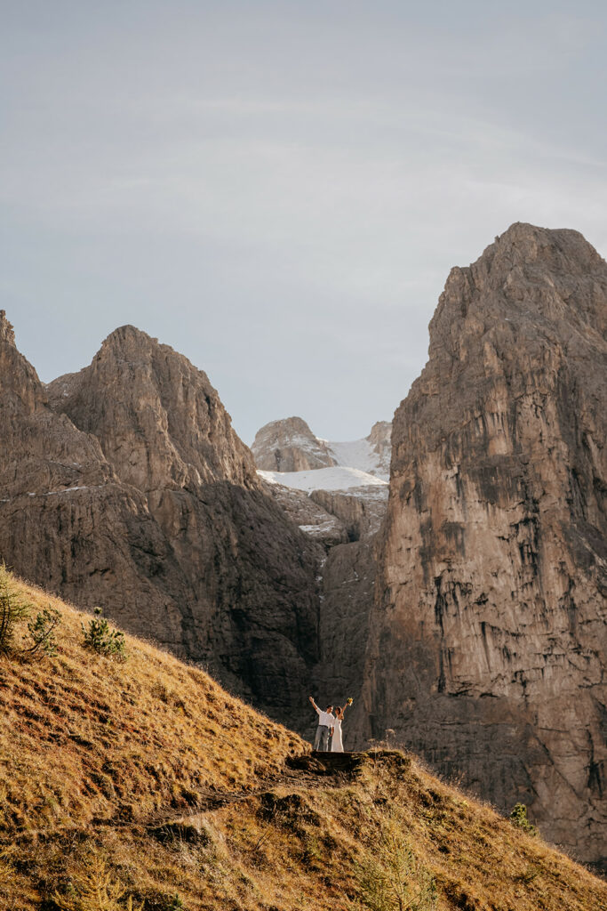 Couple celebrates on mountain path with rocky backdrop.