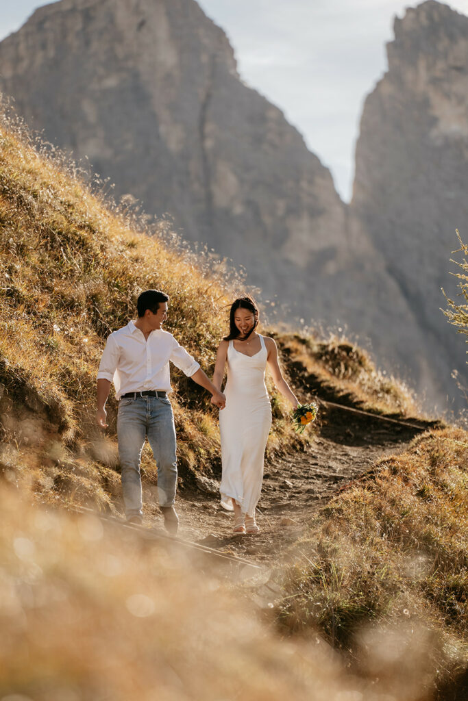 Couple hiking in mountains, holding hands, sunny day.