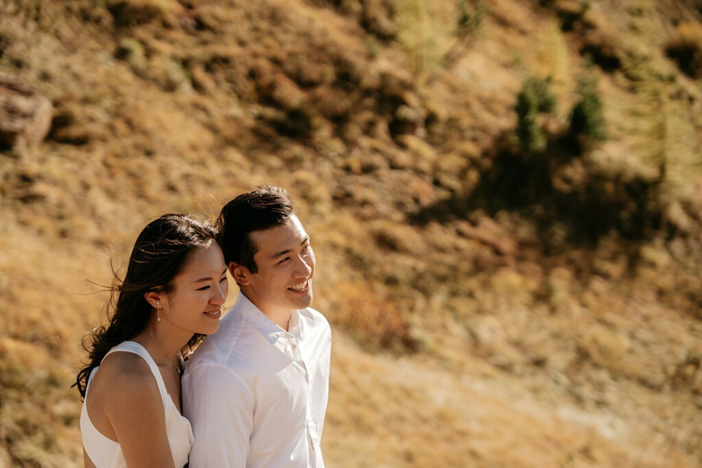 Couple smiling outdoors, sunlit landscape background.
