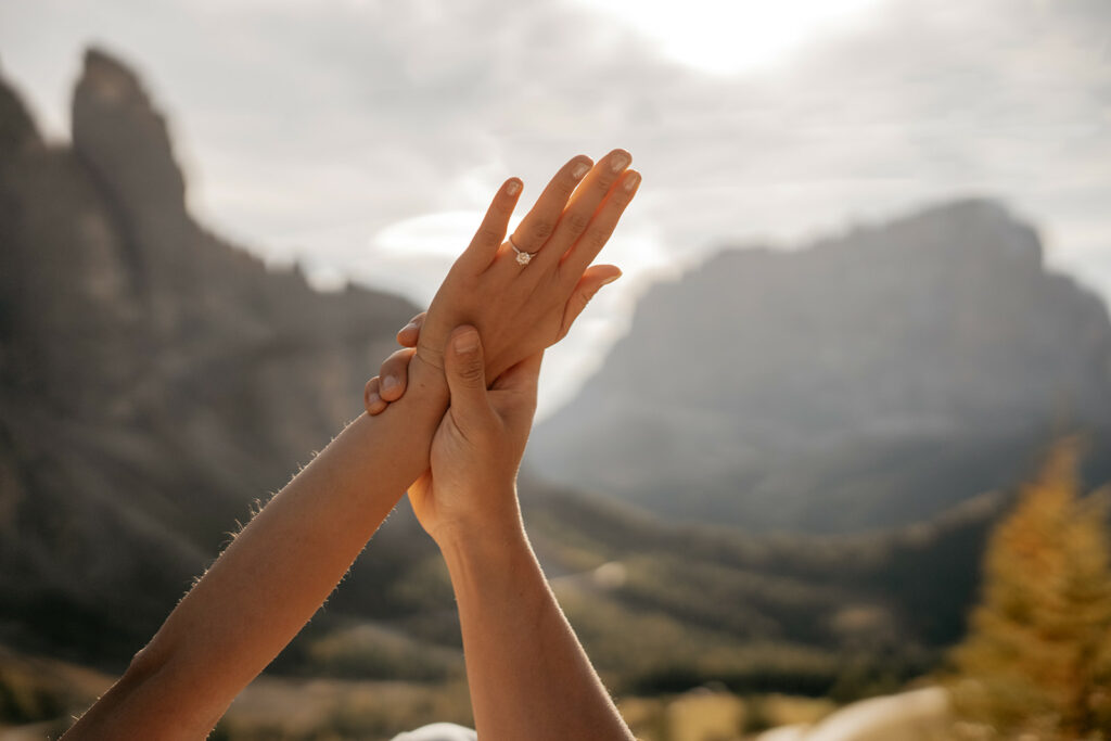 Hands holding engagement ring against mountain backdrop.