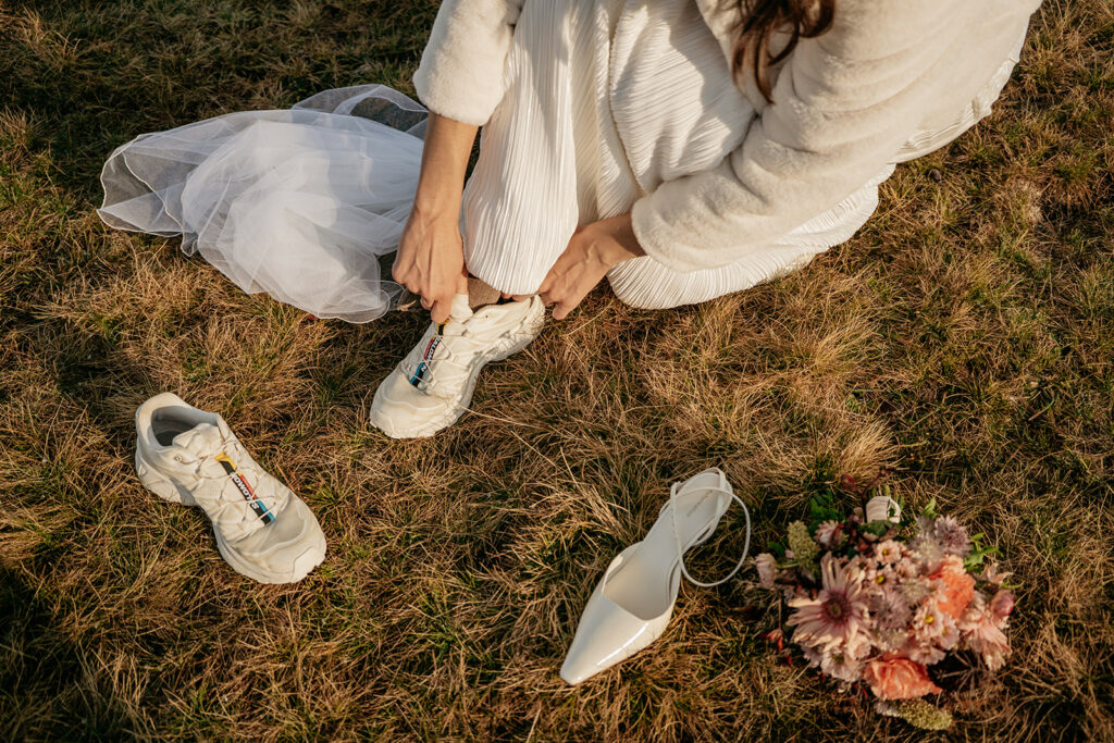 Bride changing shoes, holding laced sneakers