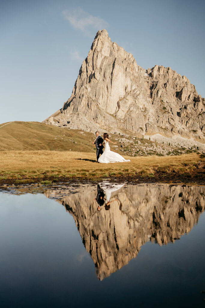Bride and groom near mountain reflected in lake