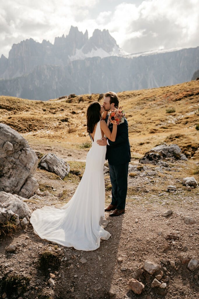 Bride and groom kiss in mountain landscape.