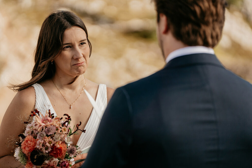 Bride holding bouquet, listening to groom outdoors