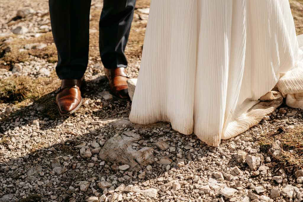 Bride and groom's shoes on rocky ground.