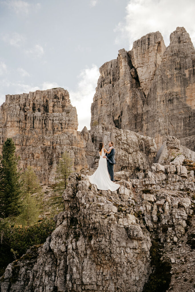 Bride and groom stand on rocky mountain cliff.