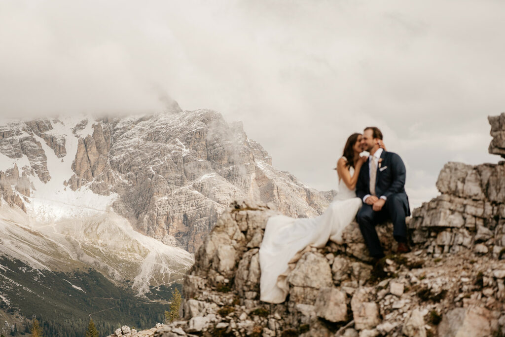 Couple sitting on rocky cliff, mountain background.