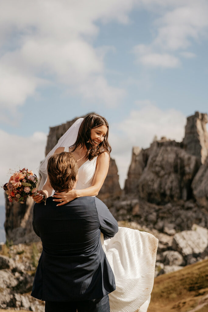 Bride carried by groom in mountain landscape.
