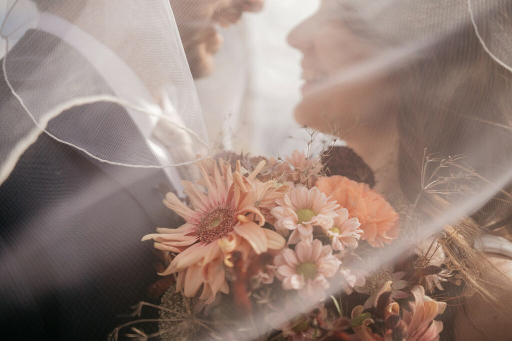 Bride and groom under veil with bouquet