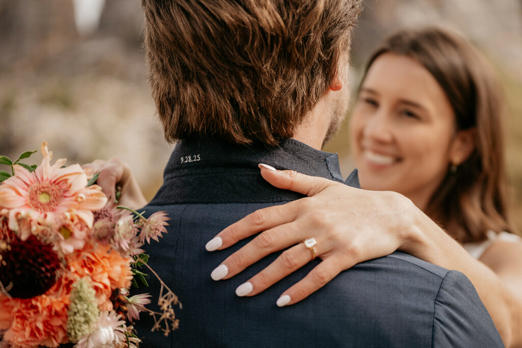 Couple embracing with flowers and engagement ring visible.
