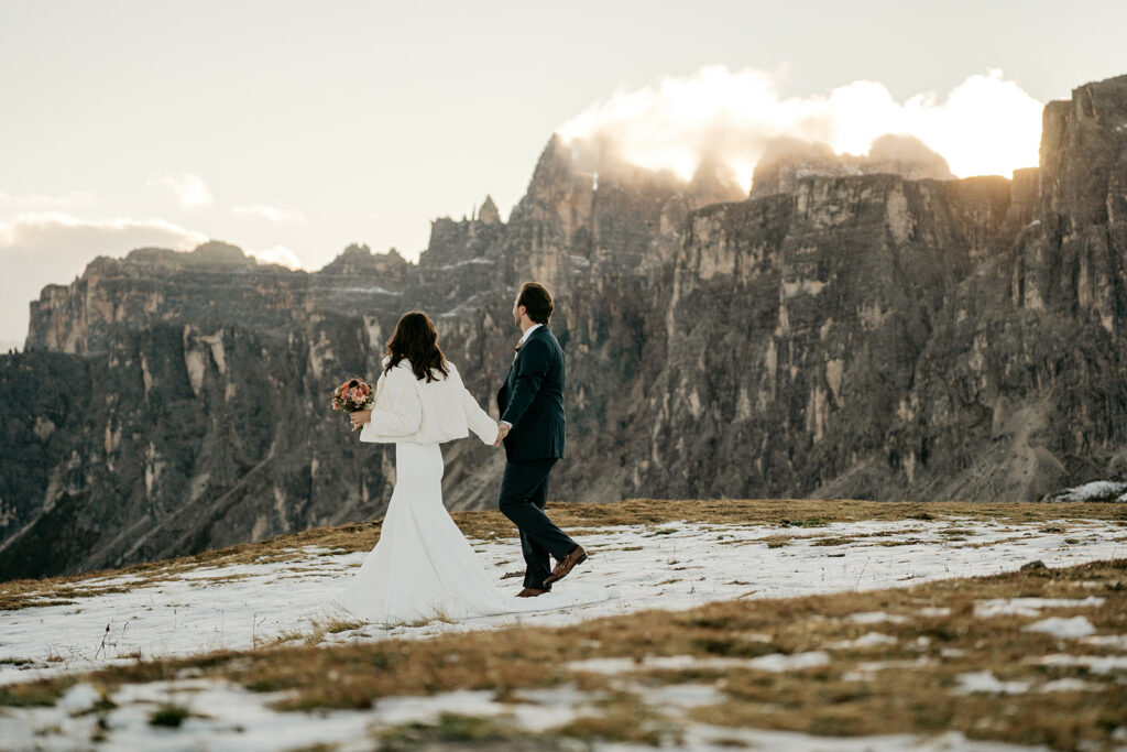 Couple walking on snowy mountain during sunset.