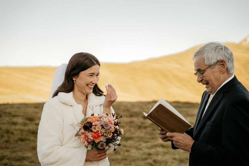 Smiling bride with bouquet and officiant outdoors.