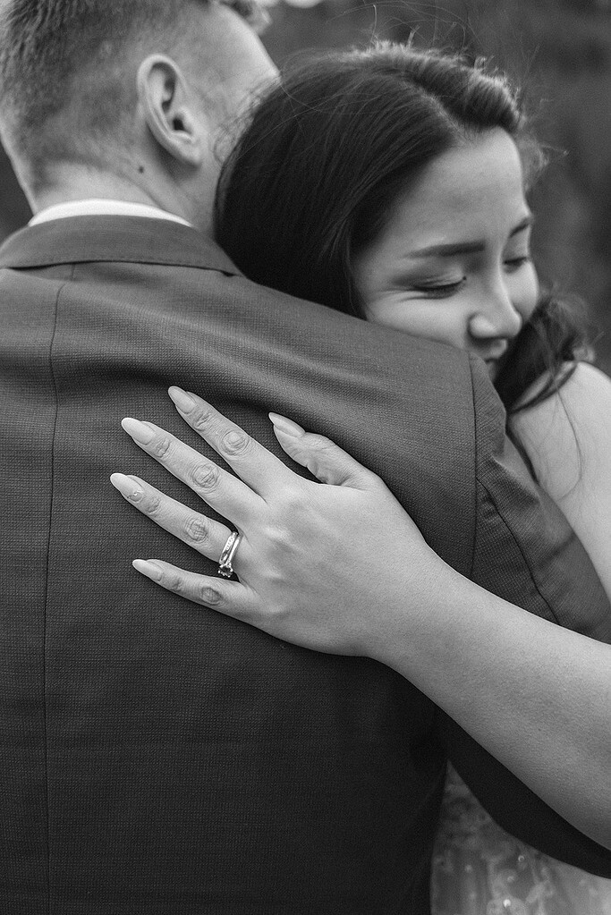 Smiling woman hugs man, hand with ring visible.