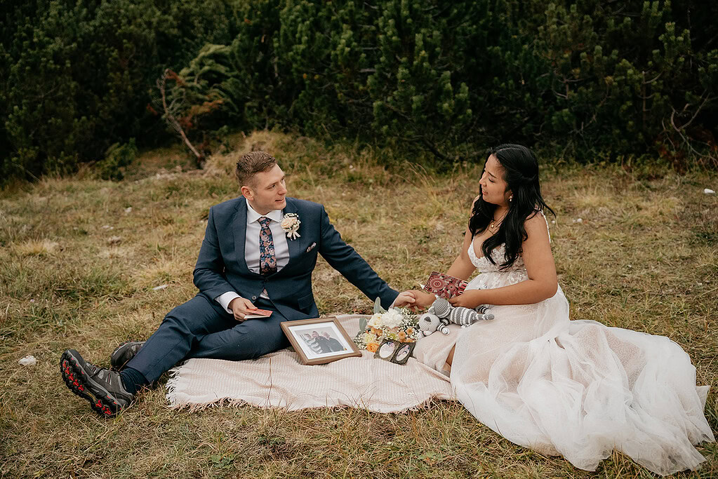 Bride and groom seated on a picnic blanket.