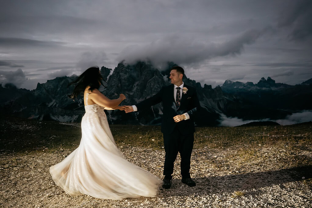 Couple dancing on mountain with dramatic sky background.