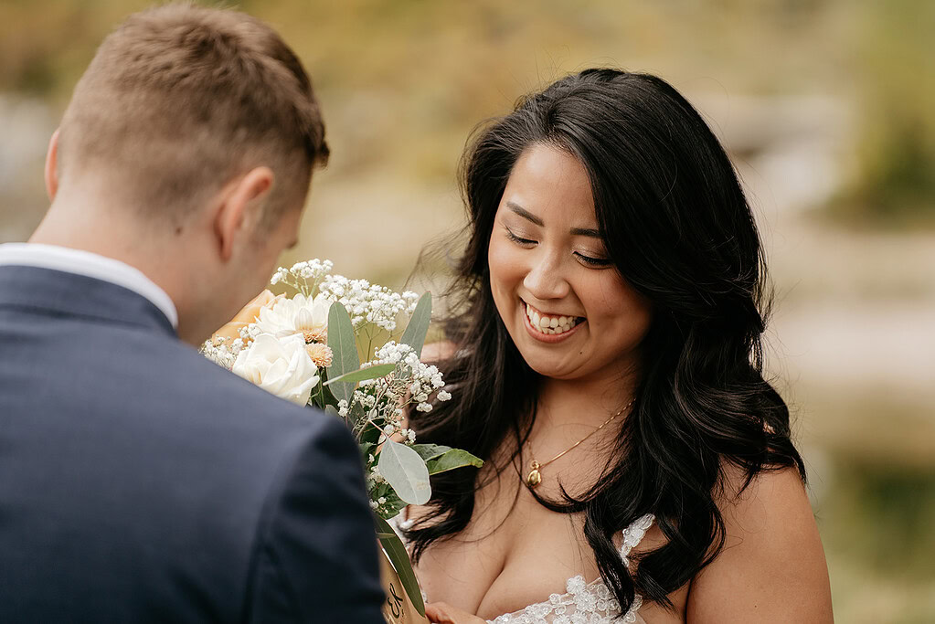 Smiling bride with bouquet during outdoor ceremony.