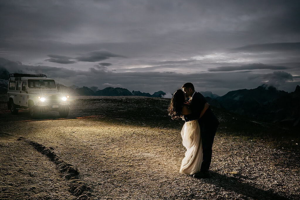 Couple kissing by car in mountainous landscape at dusk.