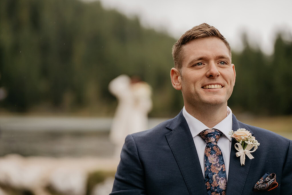 Groom smiling outdoors with trees in background.