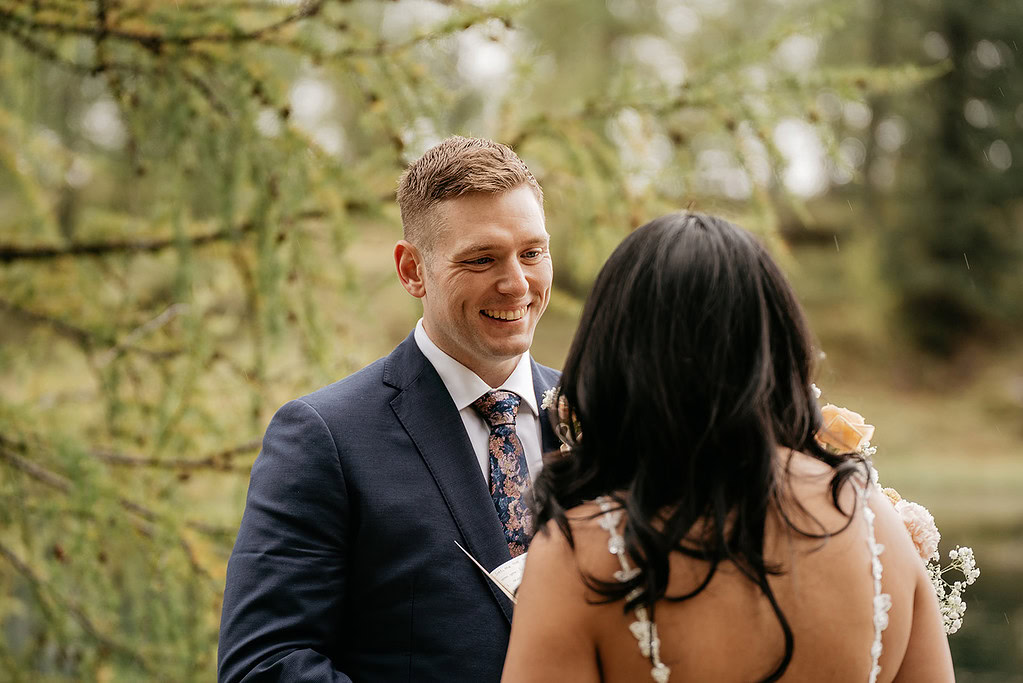 Bride and groom smiling during outdoor wedding ceremony.