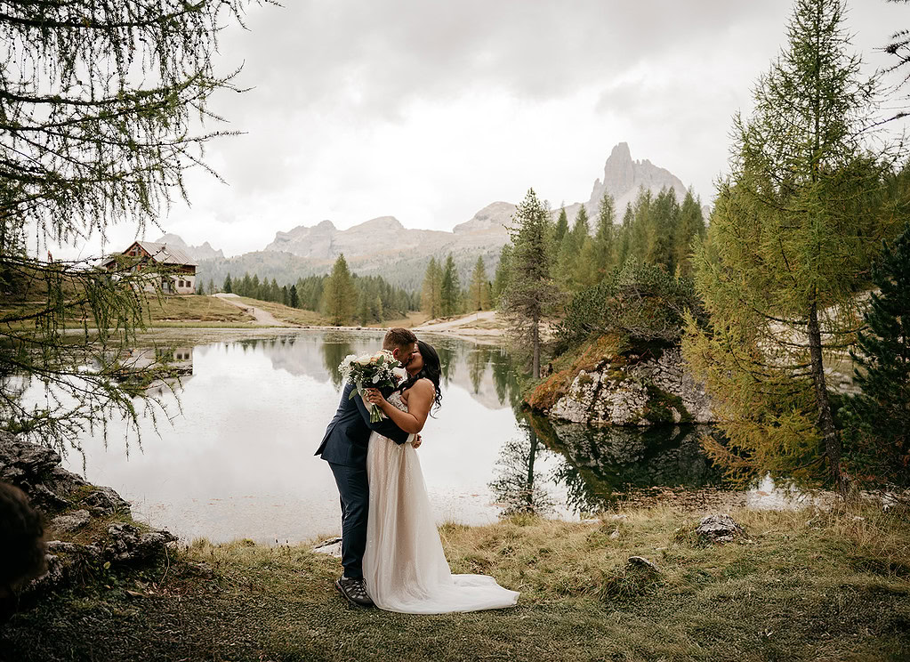 Couple kissing by mountain lake, wedding scene.