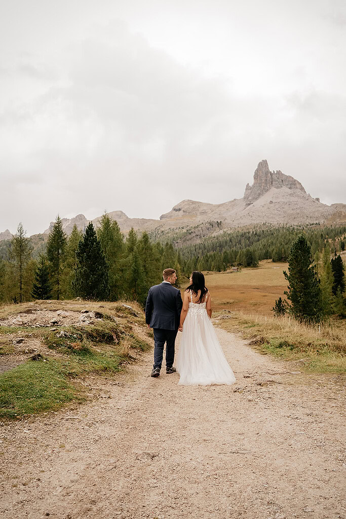 Couple walking on mountain path in wedding attire.