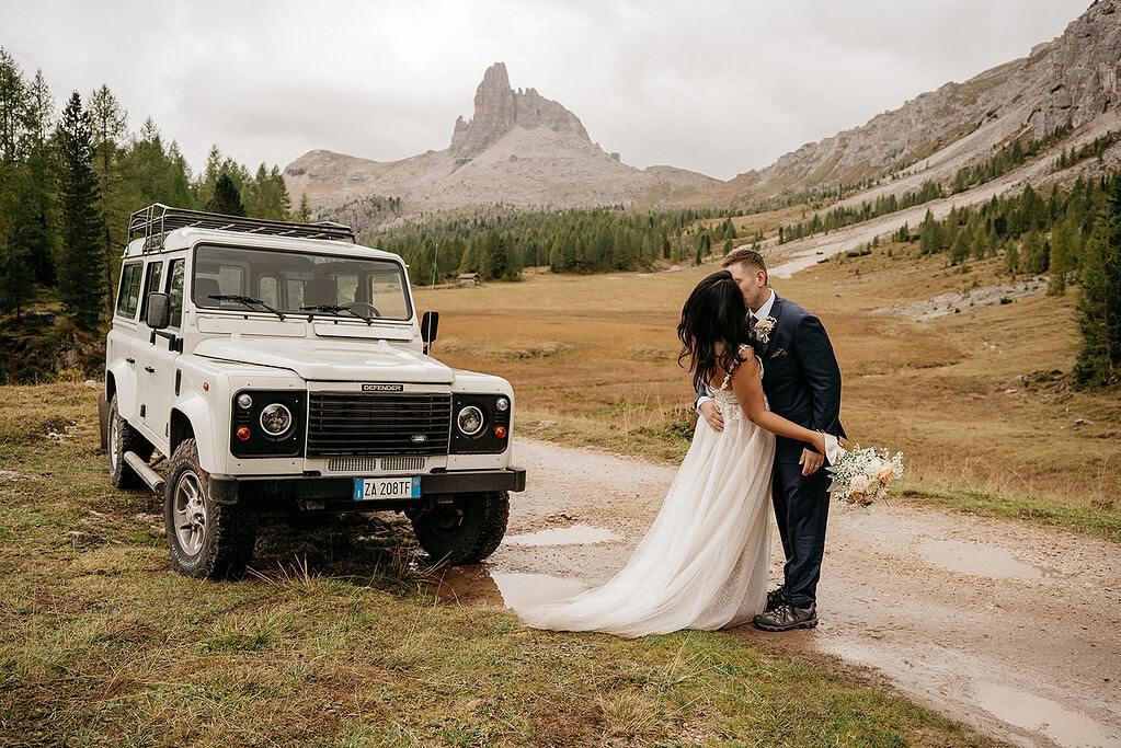 Couple kissing by Land Rover in scenic mountain.