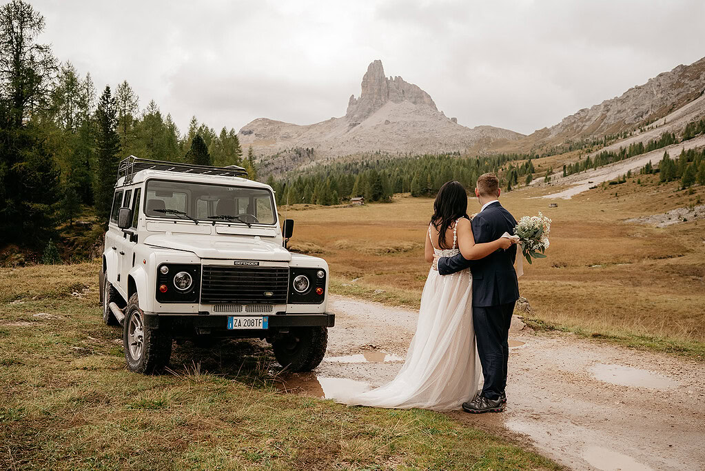 Wedding couple with SUV in scenic mountain landscape.