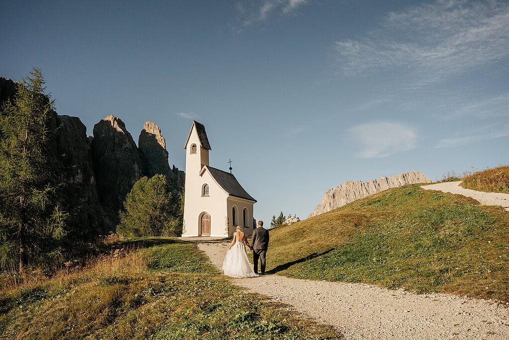 Bride and groom walking to mountain chapel.