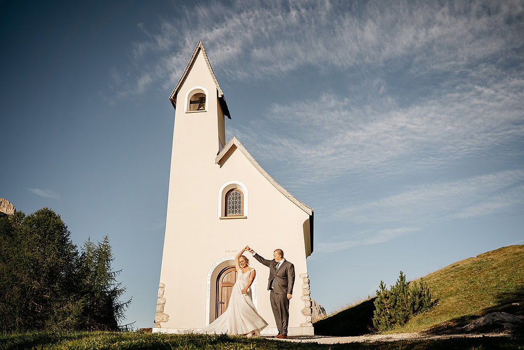 Couple dancing outside small church under blue sky.