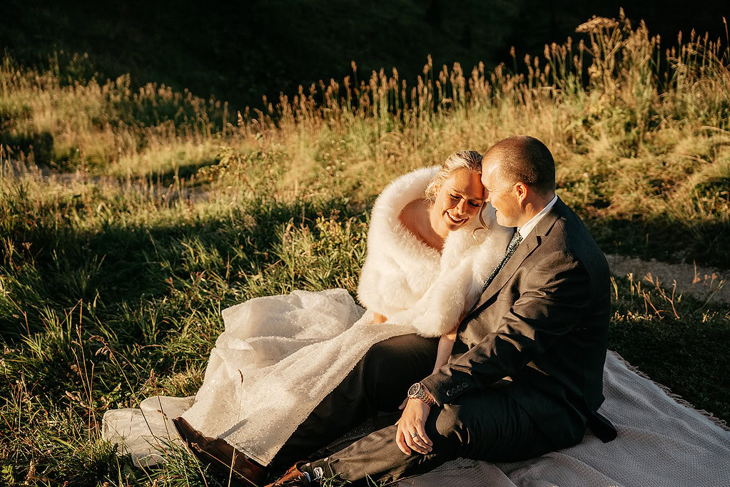 Couple sitting together on grassy field at sunset.