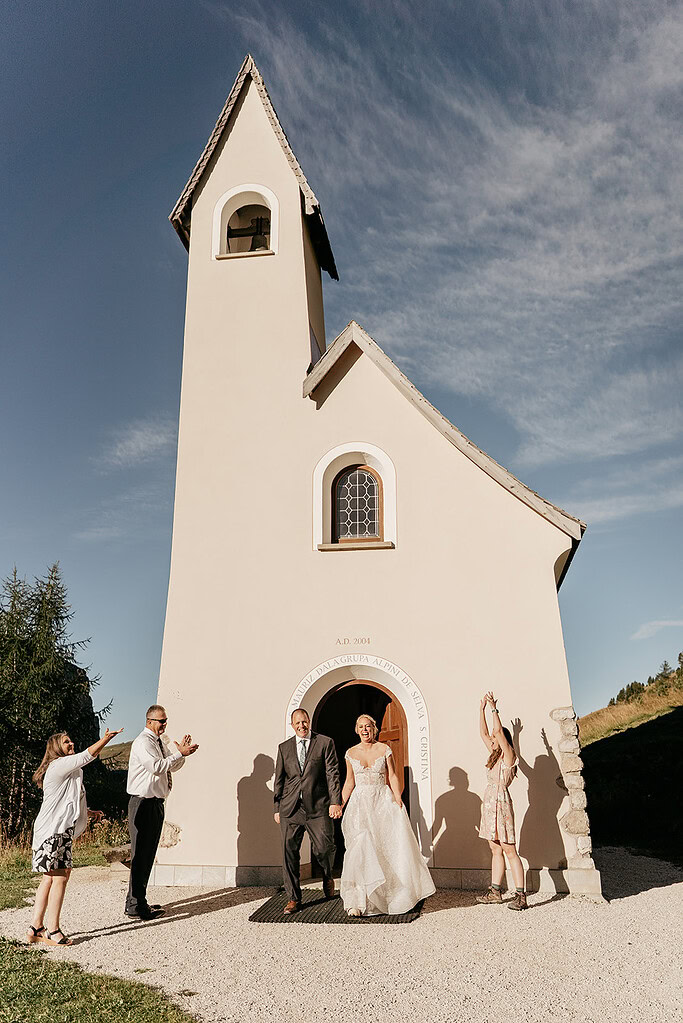 Bride and groom leaving small beige chapel.