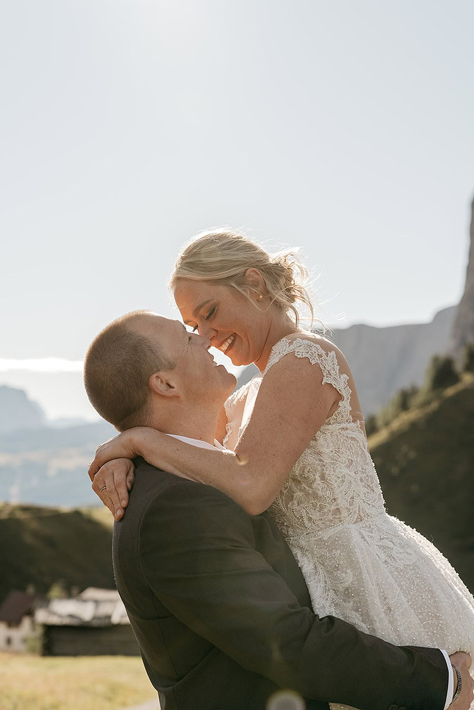 Bride and groom embracing outdoors in sunlight.