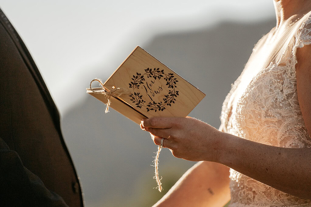 Bride holds engraved wooden vow book outdoors.