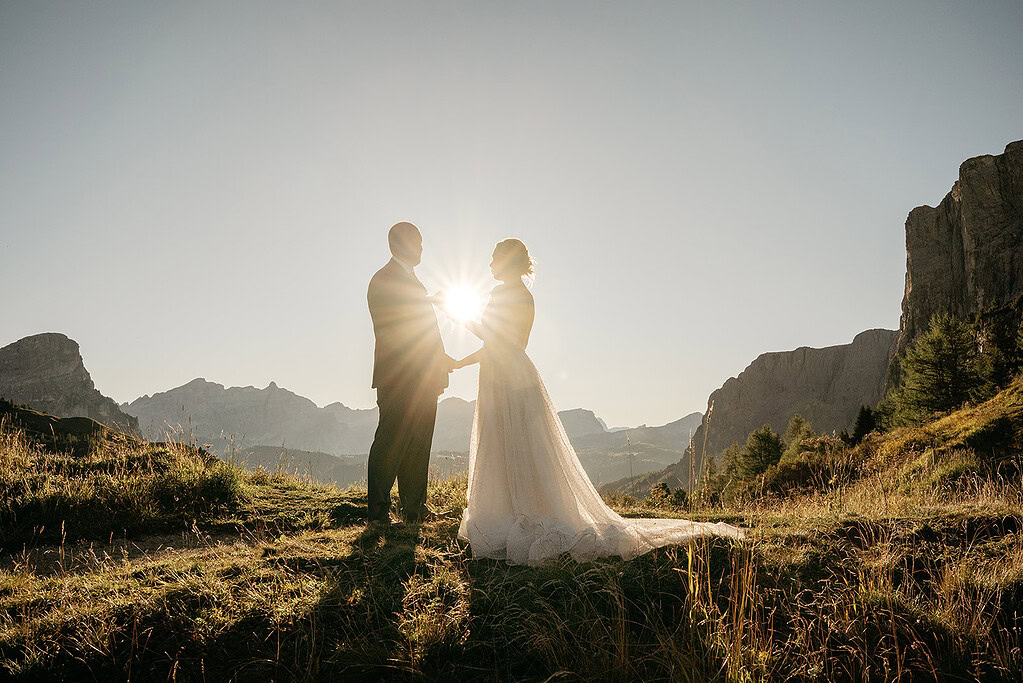 Wedding couple backlit by sunset in mountains.